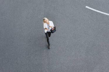 Geschäftsfrau mit Smartphone beim Gehen auf der Straße in der Stadt - DIGF11382
