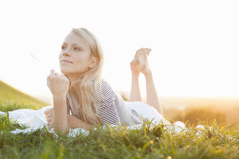 Thoughtful young woman lying on blanket against clear sky in park during sunset stock photo