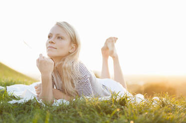 Thoughtful young woman lying on blanket against clear sky in park during sunset - DIGF11387
