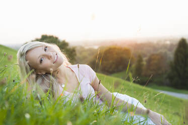 Lächelnde junge schöne Frau liegt auf grasbewachsenen Land gegen klaren Himmel bei Sonnenuntergang - DIGF11390