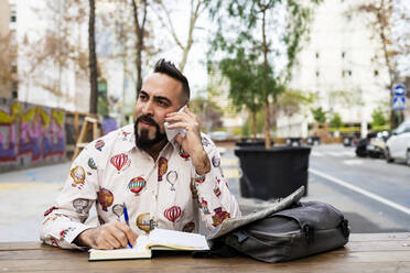 Young bearded businessman sitting at table,using mobile phone - CAVF81982