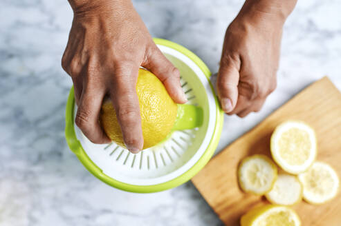 Hände einer Frau beim Auspressen von Zitronen mit einer Saftpresse - KIJF03024