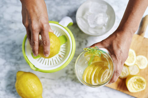 Hände einer Frau beim Auspressen von Zitronen mit einer Saftpresse - KIJF03025