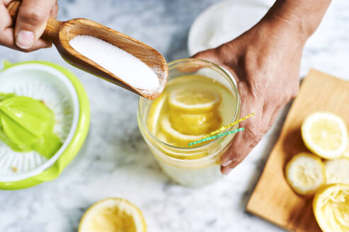 Hände einer Frau, die Zucker in einen Krug mit selbstgemachter Limonade gibt - KIJF03030