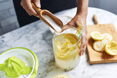 Hände einer Frau, die Zucker in einen Krug mit selbstgemachter Limonade gibt - KIJF03031