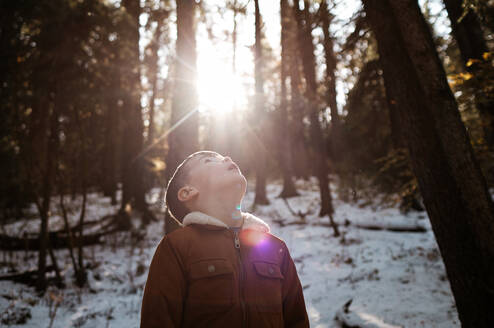 Junge im Wald, der im Winter in die Sonne schaut - CAVF81994