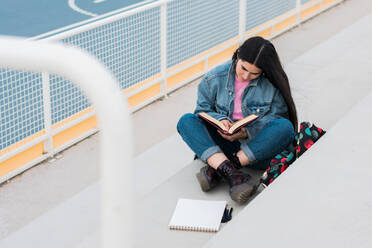 Junge Studentin liest und macht sich Notizen auf dem Campus - CAVF82009