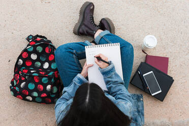 Draufsicht auf eine Studentin beim Schreiben in ihrem Notizbuch - CAVF82014