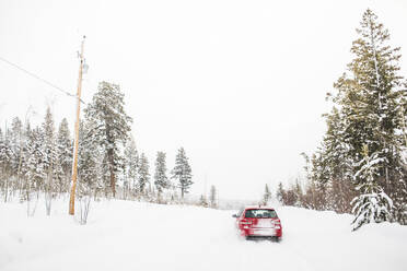 Rear view of red hatchback car driving on snow covered road. - CAVF82030
