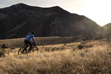 Junge Frau Mountainbike bergauf während Sonnenuntergang in den Bergen - CAVF82101