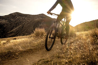 Frau beim Mountainbiken während des Sonnenuntergangs in den Bergen auf einem Singletrail - CAVF82102