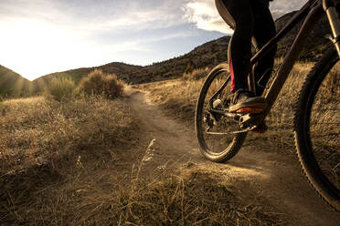 Junge Frau beim Mountainbiken während des Sonnenuntergangs in den Bergen - CAVF82103