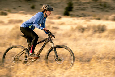 Woman riding downhill mountain biking during sunset - CAVF82104