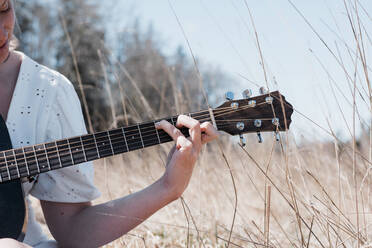 View of woman's hand playing guitar in a field in summer - CAVF82114