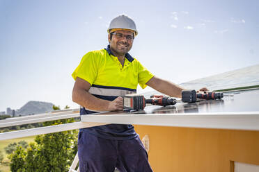 Porträt eines lächelnden reifen Technikers, der ein Solarpanel auf einem Hausdach gegen den Himmel installiert - DLTSF00700