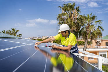 Älterer Techniker bei der Installation eines Solarpanels auf dem Hausdach gegen den Himmel an einem sonnigen Tag - DLTSF00702