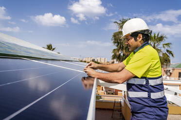 Älterer Techniker bei der Installation eines Solarpanels auf dem Hausdach gegen den Himmel - DLTSF00704