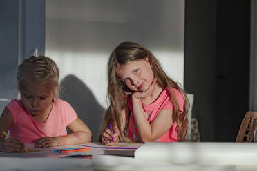 Happy girl sitting with sister coloring on paper at home - OGF00427