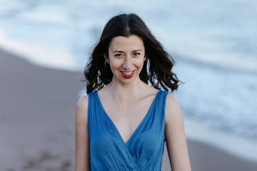 Dunkelhaarige Frau in blauem Kleid am Strand, lächelnd, Porträt - TCEF00691