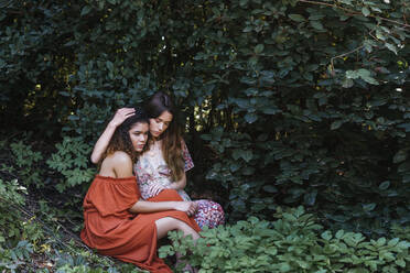 Zwei schöne Frauen sitzen in der Natur und umarmen sich - TCEF00699
