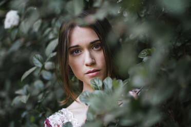 Beautiful woman looking through green leaves - TCEF00700