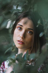 Beautiful woman looking through green leaves - TCEF00701