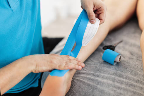 Sehbehinderter Physiotherapeut klebt in der Klinik Kinesio-Tape auf die Hand eines Jungen - MRRF00063