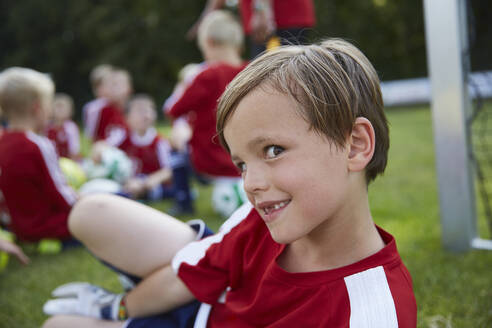 Porträt eines verspielten Jungen mit einer Fußballmannschaft im Hintergrund auf einem Feld - AUF00505