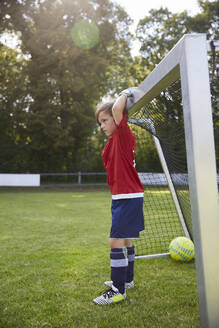 Boy in soccer uniform holding goal post at field - AUF00506