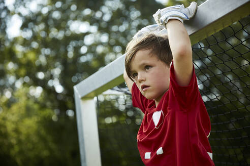 Thoughtful soccer boy holding goal post at field - AUF00507