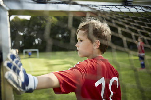 Ernster Junge in Fußballuniform hält Torpfosten auf dem Spielfeld - AUF00508