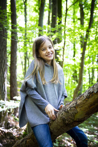 Porträt eines lächelnden niedlichen Mädchens, das auf einem Baumstamm im Wald sitzt, lizenzfreies Stockfoto