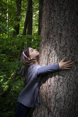 Cute elementary girl hugging tree trunk in forest stock photo