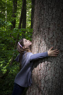 Cute elementary girl hugging tree trunk in forest - LVF08906