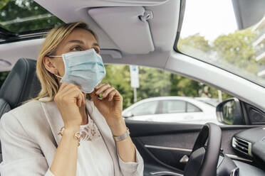 Portrait of woman in car putting on protective mask - MFF05584