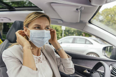 Porträt einer Frau im Auto, die eine Schutzmaske aufsetzt - MFF05585