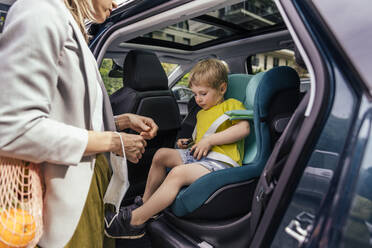 Kleiner Junge beim Befestigen der Sitzglocke des Kindersitzes im Auto, während seine Mutter ihn beobachtet - MFF05589