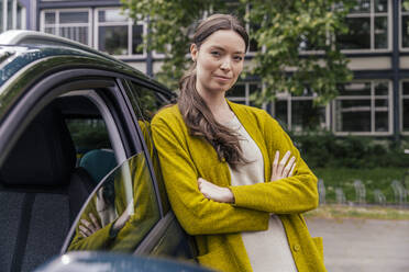 Porträt einer jungen Frau mit verschränkten Armen, die sich an ihr Auto lehnt - MFF05596