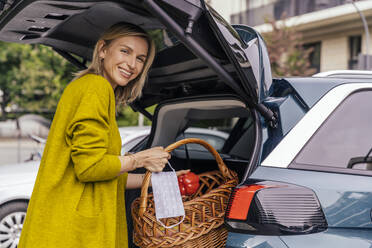 Portrait of happy woman with protective mask putting purchase in trunk of her car - MFF05609