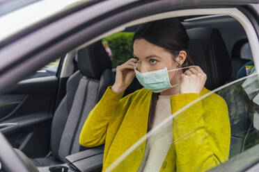 Porträt einer Frau im Auto, die ihre Schutzmaske abnimmt - MFF05610