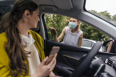 Frau mit Schutzmaske spricht durch ein Autofenster mit einer Frau ohne Maske - MFF05616