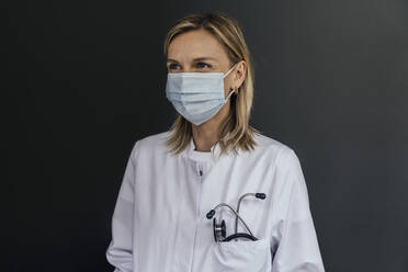 Porträt eines Arztes mit Schutzmaske vor grauem Hintergrund - MFF05622