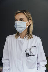 Portrait of doctor wearing protective mask against grey background - MFF05623