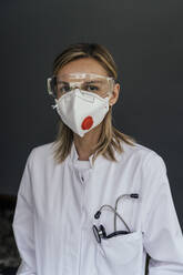 Portrait of doctor wearing FFP3 mask and safety glasses against grey background - MFF05625