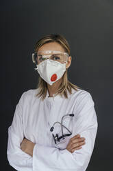 Portrait of doctor wearing FFP3 mask and safety glasses against grey background - MFF05626