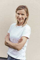 Portrait of smiling blond woman standing in front of light wall - MFF05632