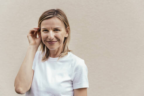 Portrait of smiling blond woman wearing white t-shirt in front of light wall - MFF05633
