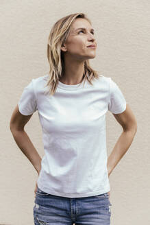 Portrait of blond woman wearing white t-shirt in front of light wall looking up - MFF05634