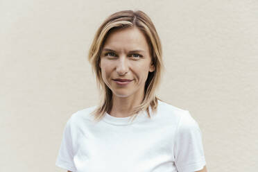 Porträt einer lächelnden blonden Frau mit weißem T-Shirt vor einer hellen Wand - MFF05636