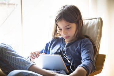 Mädchen sieht sich ein Online-Video an, während sie zu Hause auf einem Sessel am Fenster sitzt - LVF08910
